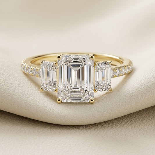 Yellow gold ring with emerald cut center stone and side diamonds
Elegant three stone diamond ring featuring rectangular step cut gems
Luxury gold engagement ring with large emerald cut centerpiece
Sparkling three stone ring with diamond accented yellow gold band
Classic emerald cut diamond ring with matching side stones
Fine jewelry gold ring featuring a bold rectangular center diamond
Designer three stone diamond ring displayed on an ivory surface
Sophisticated yellow gold ring with step cut diamond arrang