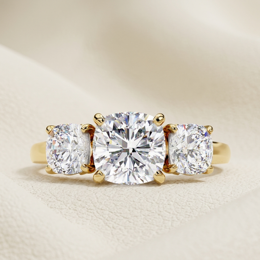 Three stone cushion cut diamond ring in yellow gold
Cushion cut three stone diamond engagement ring
Yellow gold three stone diamond ring close-up
Luxury cushion cut diamond trilogy ring
Fine jewelry three stone cushion diamond ring
Elegant cushion cut engagement ring with side diamonds
Modern three stone diamond solitaire ring
Premium cushion cut diamond ring product photo
Classic three stone diamond engagement ring
Timeless cushion cut trilogy diamond ring